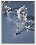 Diamond cross pendant necklace styled beside a martini glass on a steel blue background